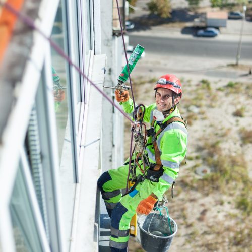 Cheerful industrial climber on building during winterization works, looking up at camera and smiling