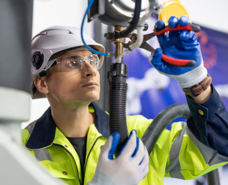 Male engineer using combination pliers tool repair robot arm welding machine in factory. Technician automation robot in uniform working at robot industrial.